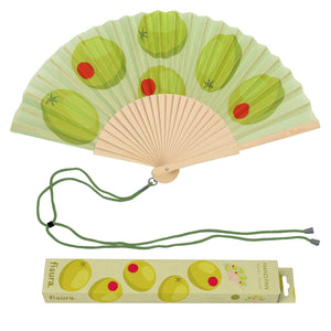 Handheld fan with wooden ribs and a green and red olive design on a green background. The fan is attached to a green lanyard to wear around your neck. The packaging box for the fan sits underneath it, featuring illustrations of olives along with the company branding. 