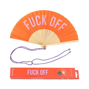 Handheld fan with wooden ribs and an orange coloured design with the text 'FUCK OFF' in pink. The fan is attached to a green lanyard to wear around your neck. The packaging box for the fan sits underneath it.