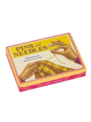 Image of a pocket storage tin featuring a vintage style illustration of someone holding a needle and sewing an item. The text 'Pins and Needles' and 'I like when my shit turns out cool' is printed on the top.