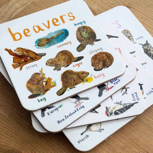 Coaster featuring illustrations of beavers on a white background. Each beaver is labelled, while the text 'Beavers' is printed on the top. The coaster sits on top of some other coasters on a wooden surface. 