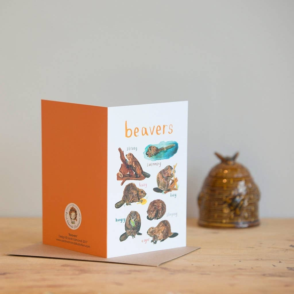 Greeting card featuring beaver illustrations on a white background. The heading 'Beavers' is printed at the top of the card while each of the illustrations is labelled with smaller text. The card sits on a wooden surface on top of a brown envelope. 