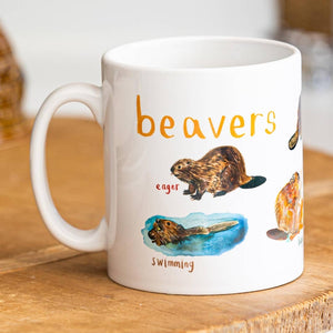 A mug with beaver illustrations on a white background. The text 'Beavers' is printed over the illustrations along with text labelling each image. The mug sits on a wooden surface.