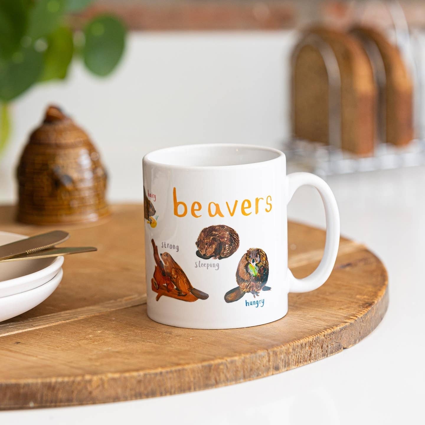 A mug with beaver illustrations on a white background. The text 'Beavers' is printed over the illustrations along with text labelling each image. The mug sits on a wooden surface.