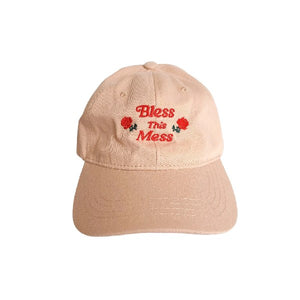 beige dad hat with an embroidered design. centred red text reads "bless this mess". two red roses frame the word "this"
