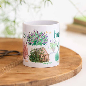 A white mug with colourful illustrations of different types of bushes. Each image is labelled with text and the mug sits on a wooden surface.