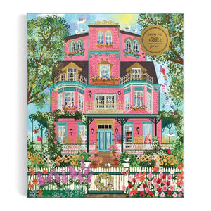 Jigsaw puzzle box with a colorful illustration of a pink house and flower filled garden on a white background.