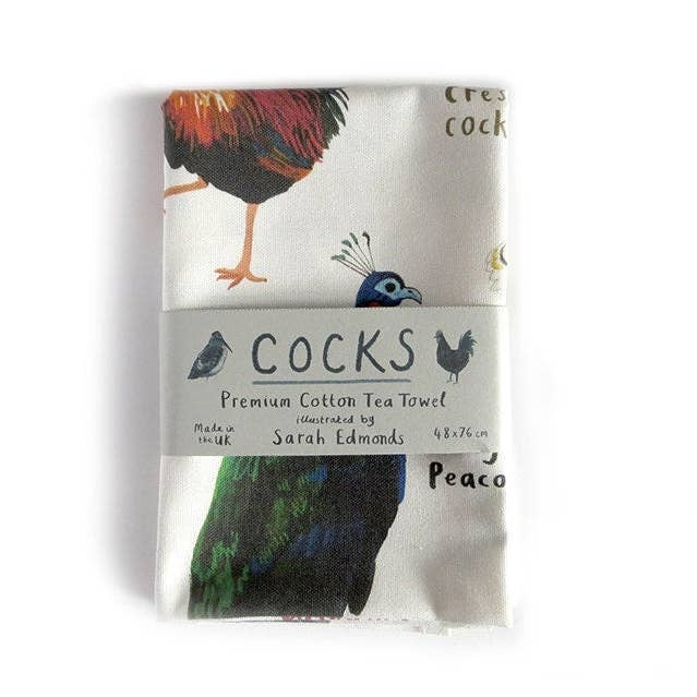 A folded cotton tea towel with a humorous bird-themed print featuring different types of cock birds, wrapped in a paper band that reads 'Cocks' and 'Premium Cotton Tea Towel'.