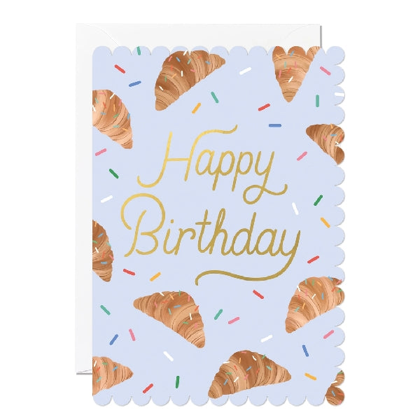 Greeting card with a scalloped edge featuring croissant designs on a blue background with the text 'Happy Birthday'. 
