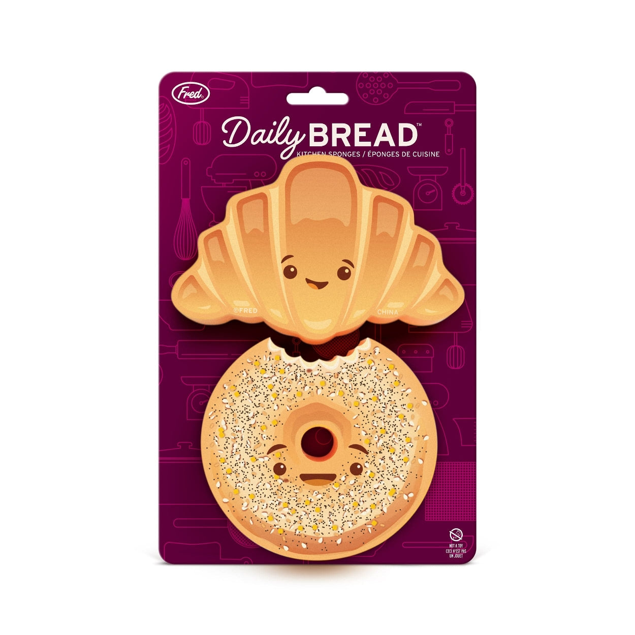 Two smiling bread-themed kitchen sponges in their packaging. One is in the style of a croissant, while the other is a bagel. The purple packaging shows the text 'Daily Bread', the company branding and shows some illustrations of kitchen appliances in the background.
