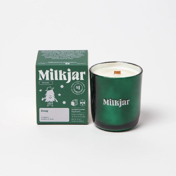 Canadian company Milkjar candle and its box packaging. The white candle is in a green glass with "Milkjar" written in grey. The other side of the candle has a cute smiling pine tree with a hat and legs doodle in grey. The packaging is a small green box with grey text and graphics. 
