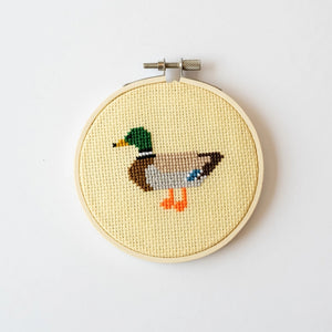 Cross-stitched duck design contained in a wooden hoop against a white background.