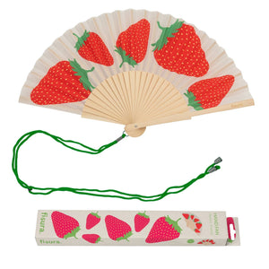 Handheld fan with wooden ribs and a red and green strawberry design on a white background. The fan is attached to a green lanyard to wear around your neck. The packaging box for the fan sits underneath it, featuring illustrations of strawberries along with the company branding. 