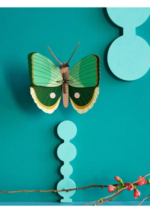 3D decorative butterfly hanging on a teal background with floral elements.