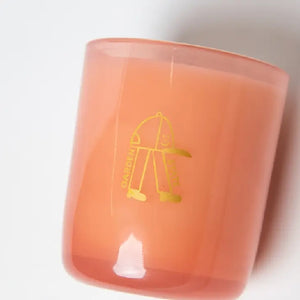 White candle in an orange glass with "Garden state" written in yellow. alongside a cute smiling baseball hat with legs doodle in yellow. The candle is on a white background.