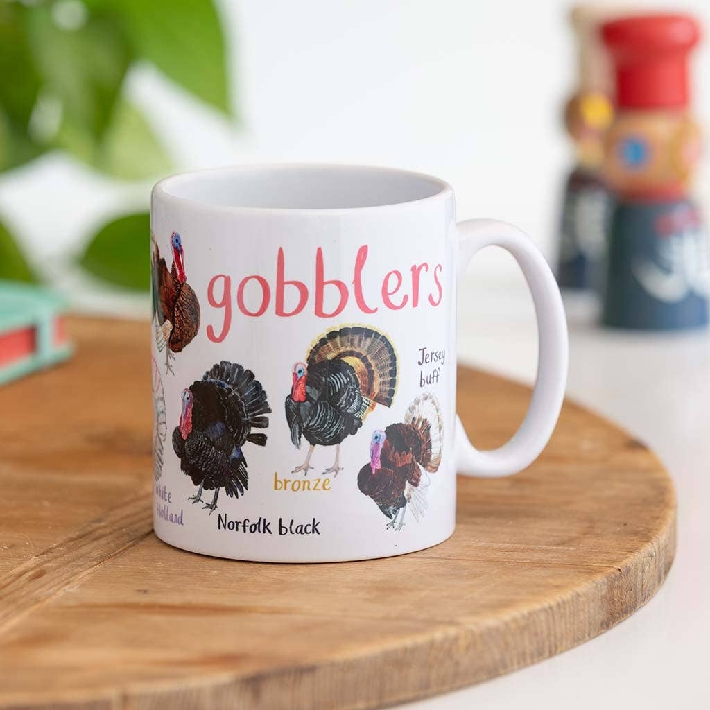 A mug with turkey illustrations on a white background. The text 'Gobblers' is printed over the illustrations along with text labelling each image. The mug sits on a wooden surface.