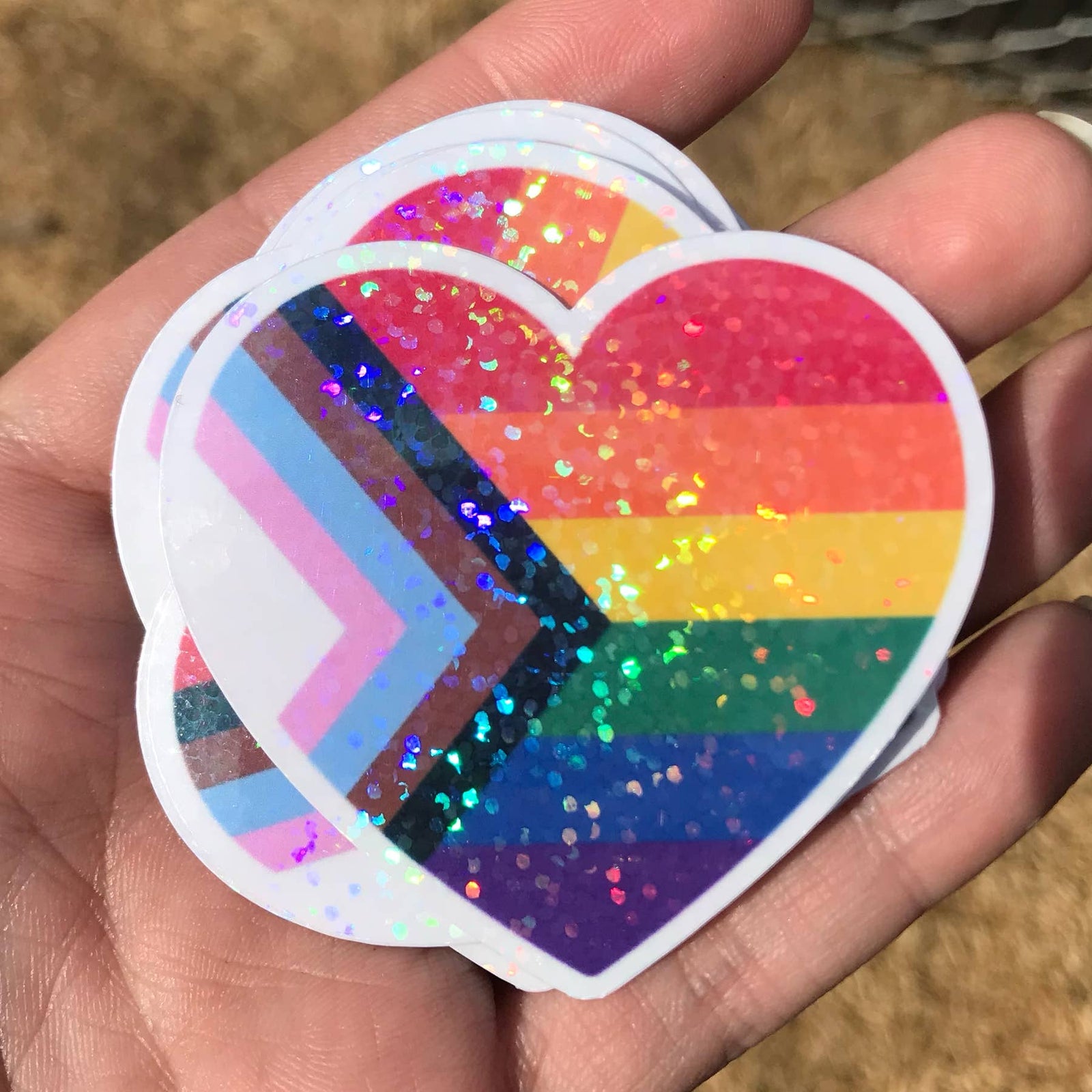 A heart shaped sticker with a white border. The inside of the heart is filled with the colours of the Pride flag, but with sparkles.