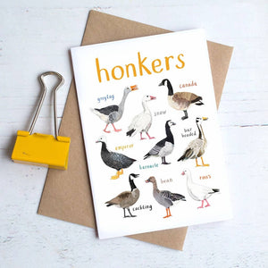 Greeting card featuring illustrations of geese on a white background. The heading 'honkers' is printed at the top of the card while each of the images are labelled with smaller text. The card lies on top of a brown envelope on a white surface. 