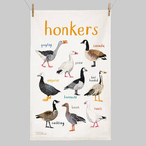 A white cotton tea towel showing colourful bird illustrations with text  printed underneath. The heading 'honkers' is printed at the top of it. The tea towel hangs from 2 clips on a string. 