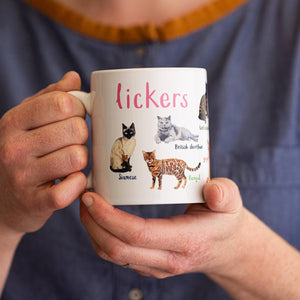 Person holding a white mug with labelled cat illustrations and the text 'Lickers'.