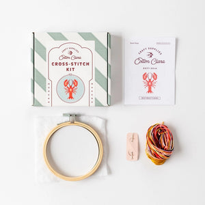 Lobster themed cross-stitch kit with a hoop, coloured threads, and packaging on a white background.