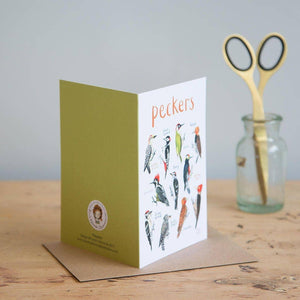 Greeting card featuring bird illustrations on a white background. The heading 'Peckers' is printed at the top of the card while each of the illustrations is labelled with smaller text. The card stands on a wooden surface. 