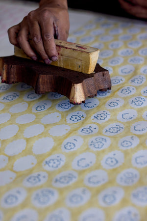 Hand using a wooden block on yellow paper with botanical patterns.