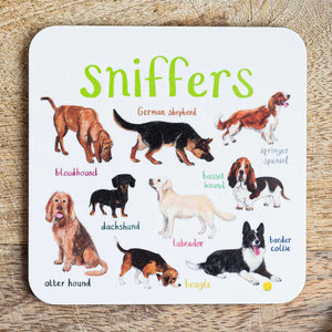 Coaster featuring illustrations of different dog breeds on a white background. Each dog is labelled with their breed while the text 'sniffers' is printed on the top. The coaster sits on a wooden surface.