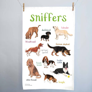 A white cotton tea towel showing dog illustrations with text printed underneath. The heading 'Sniffers' is printed at the top. The tea towel hangs from 2 wooden clips on a string. 