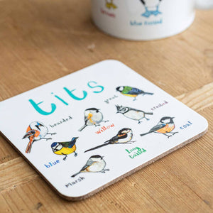 Coaster featuring illustrations of birds on a white background. Each bird is labelled, while the text 'Tits' is printed on the top. The coaster sits on a wooden surface.