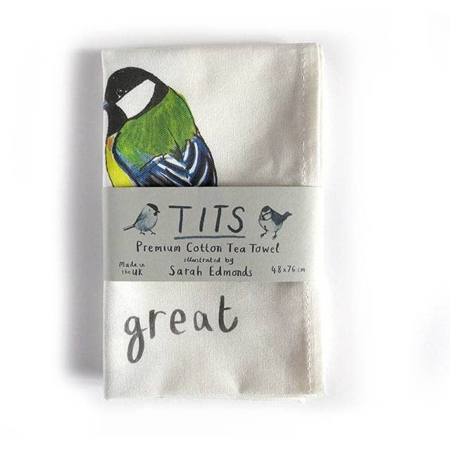 A white cotton tea towel showing an image of a colourful bird illustration with the word 'great' printed underneath. The tea towel is folded and a paper label titled 'Tits' is wrapped around the middle. 