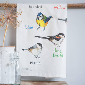 Tea towel with colourful bird illustrations and text hanging on a wooden bar.