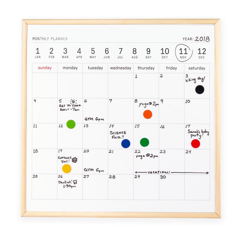 white board calendar with a pale wood frame. both printed and hadnwritten text is seen. kikkerland product on white background