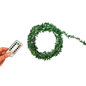 circle bundle of wire with leaves on it on a white background. a white hand holds a remote control on the left side of the image. kikkerland product